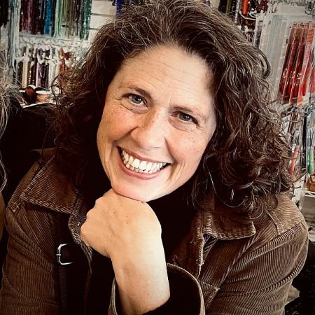 A woman smiles while holding her chin on her hand.