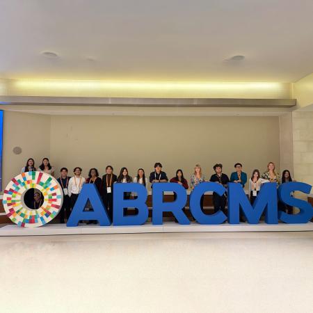 A group of students stands behind large ABRCMS letters at a conference venue.