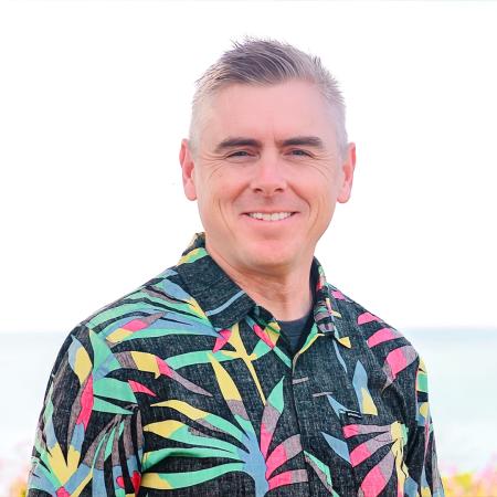 A person smiles in a posed portrait outdoors near a waterfront.