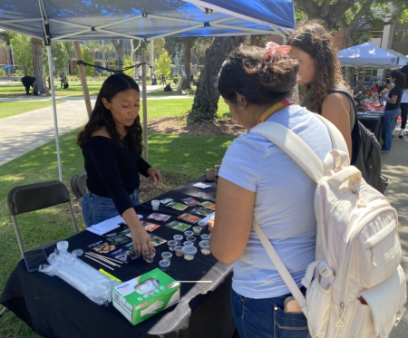 Three students standing at a table choosing seeds to plant while outside under a tent.