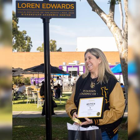 A person holds a certificate and stands next to a recognition sign outdoors