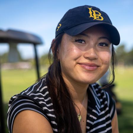 A person in a baseball cap smiles outdoors near a golf cart