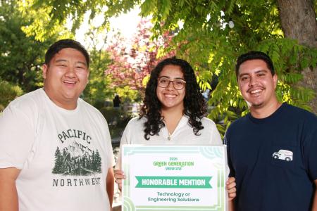 Three students standing in front of trees holding a sign