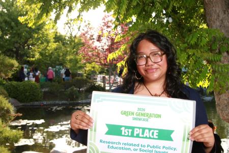 A student holding a first place sign standing in front of a tree