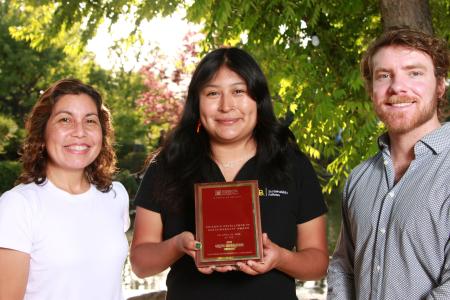 Three people standing in front of a tree and one is holding an award plaque