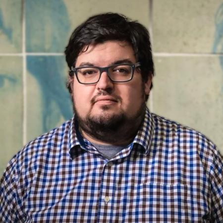 Person with beard and glasses looks into camera