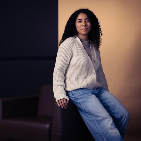 A person wearing a sweater and blue jeans leans on a chair 