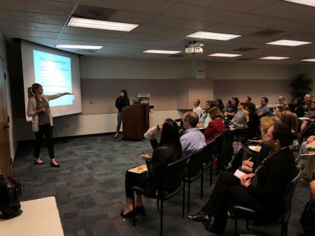a woman presenting in front of a group in a classroom