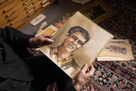 A portrait of a young person is held by two hands