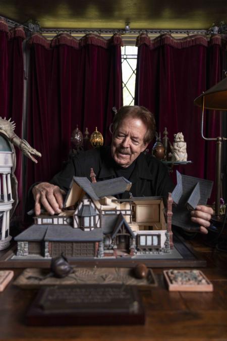 A person lifts the roof off of a model house