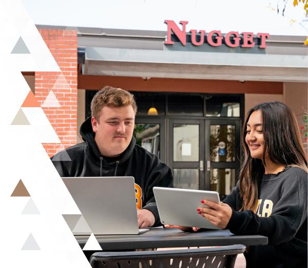 Two students studying outside the Nugget Grill and Pub looking at two tech devices. 