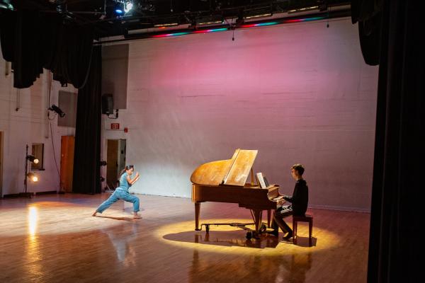 Vernice Ednilao performs a dance next to a piano player playing piano.