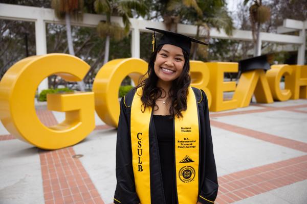 Graduating student standing of the GO BEACH sign