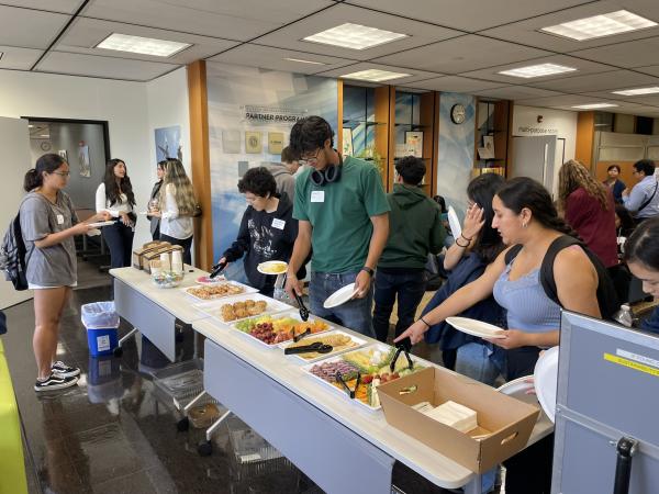 Students grabbing fruit and snacks from tables.