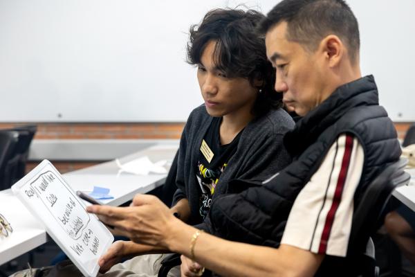 Two people sit side by side reviewing a small whiteboard