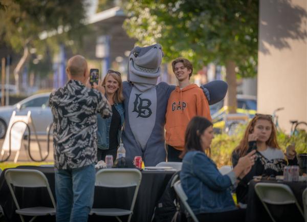 A family posing with Elbee the shark at a family event.