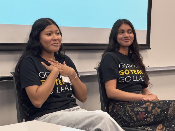 Two female students sitting in chairs talking to students