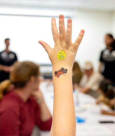 Child with sticker on hand raises hand