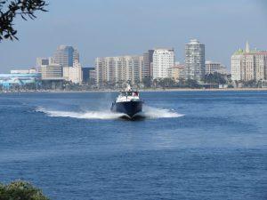Shoreline with a boat whirring forward ans the city skyline in the distance