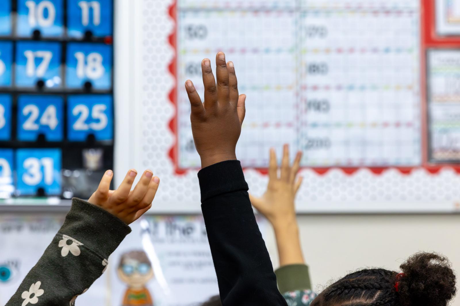 First grade students hold up their hands in a class at Mark Twain Elementary