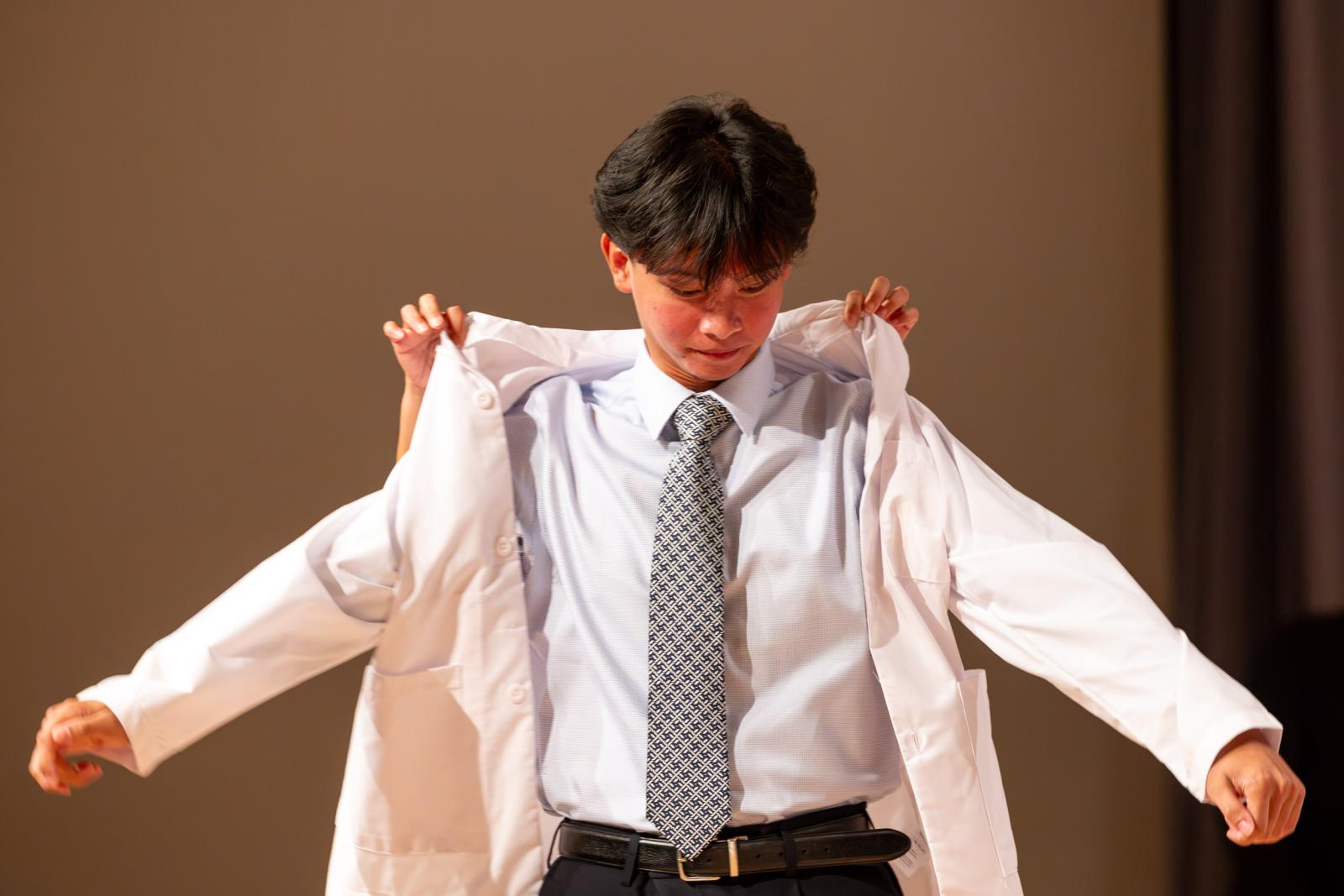 A student gets help putting on a lab coat at the 2026 White Coat Ceremony