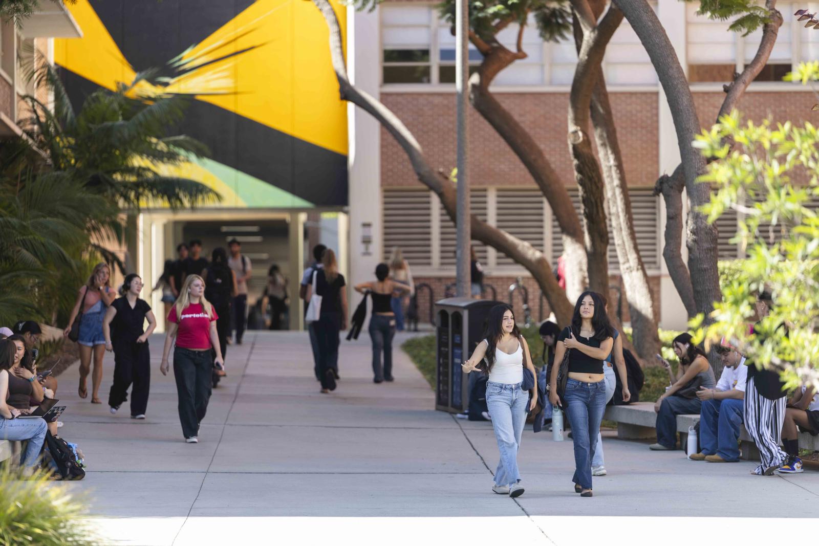 Student walking in between buildings, Rita Letendre's "Sun Forces" mural in background