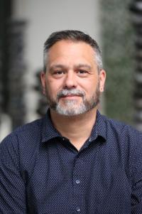 man with dark blue shirt, short grey beard and hair