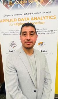 Mahmoud Albawaneh AVP for Institutional Research and Analytics Mahmoud Albawaneh wearing a light gray blazer and a light-colored shirt is standing in front of a vertical banner. The banner promotes “Applied Data Analytics for Higher Education” and includes text about shaping the future of higher education, along with icons representing real data and real code.