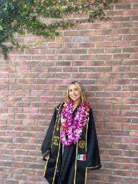 CDFS alumni wearing a graduation gown posing against a brick wall