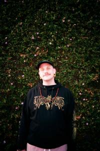 person with hat standing in front of a tall bush